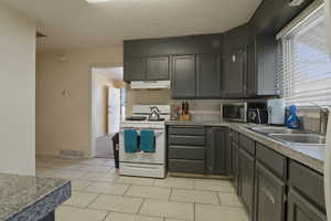 Kitchen with white gas stove, gray cabinets, stainless steel microwave, and light tile patterned flooring