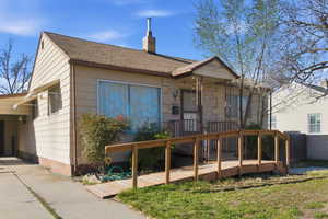 View of front of property featuring a chimney, a deck, an attached carport, and stone siding