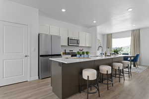 Kitchen with stainless steel appliances, a kitchen breakfast bar, a center island with sink, light wood-style floors, and recessed lighting