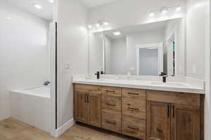 Full bathroom with double vanity, a bath, and light wood-style floors