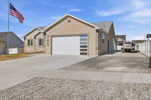 Single story home with stucco siding, driveway, stone siding, and an attached garage