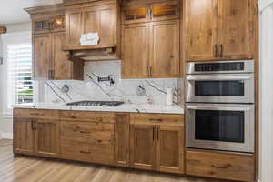 Kitchen featuring stainless steel appliances, glass insert cabinets, backsplash, and wood finish cabinetry