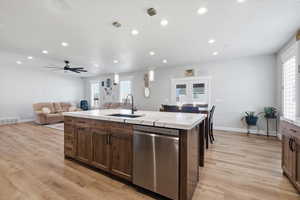 Kitchen featuring stainless steel dishwasher, an island with sink, light wood-type flooring, and open floor plan