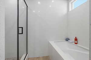 Full bath with a stall shower, a garden tub, and light wood-style flooring