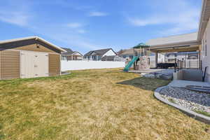 Fenced backyard with a playground, a patio area, a storage shed, and a residential view