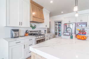 Kitchen with light stone countertops, stainless steel appliances, hanging light fixtures, and white cabinetry