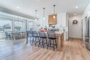 Dual tone kitchen with a kitchen breakfast bar, stainless steel appliances, two tone color scheme, light wood-style floors, and a kitchen island