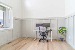Office with wainscoting, a decorative wall, and light wood-style floors