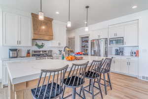 Kitchen with a kitchen island with sink, white cabinetry, stainless steel appliances, and hanging light fixtures