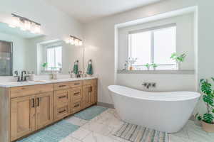 Bathroom with light marble finish flooring, double vanity, and a freestanding tub