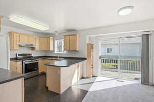 Kitchen featuring light wood finish cabinetry, gas range, dark countertops, freestanding refrigerator, and a peninsula