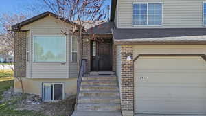 Entrance to property featuring roof with shingles, brick siding, and an attached garage