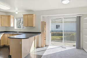 Kitchen with light wood finish cabinets, dark countertops, and a peninsula