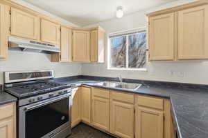 Kitchen with light wood finish cabinetry, gas stove, and dark countertops