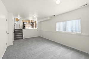 Unfurnished living room featuring stairway and light carpet