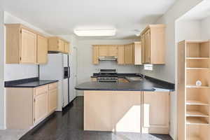Kitchen featuring light wood finish cabinets, a peninsula, stainless steel gas range, white refrigerator with ice dispenser, and dark countertops