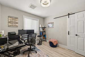 Office area featuring light wood finished floors, a barn door, and suspended lighting
