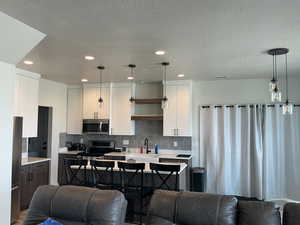 Kitchen featuring open floor plan, stainless steel appliances, a textured ceiling, decorative light fixtures, and two tone cabinets