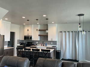 Dual tone kitchen featuring a breakfast bar, open floor plan, stainless steel appliances, dual tone cabinets, and an island with sink