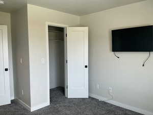 Unfurnished bedroom with dark colored carpet and a spacious closet