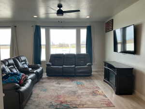 Living room with a ceiling fan, light wood-type flooring, a wood stove, a textured ceiling, and plenty of natural light