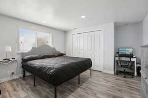 Bedroom featuring a closet, light wood-style flooring, a desk, recessed lighting, and a textured ceiling