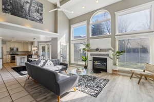 Living room featuring recessed lighting, a high ceiling, a tile fireplace, ceiling fan, and light wood-style floors