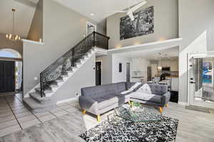 Living room with a ceiling fan, light wood-style floors, a high ceiling, and a chandelier