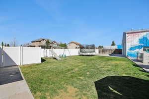 Fenced backyard featuring a trampoline, a residential view, and a playground