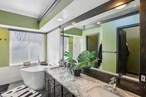Bathroom with double vanity, a freestanding bath, a textured ceiling, and recessed lighting