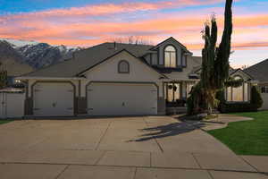 Traditional home featuring a garage, concrete driveway, stucco siding, a shingled roof, and a front yard