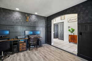 Home office featuring a wainscoted wall, a textured ceiling, wallpapered walls, light wood-type flooring, and a decorative wall
