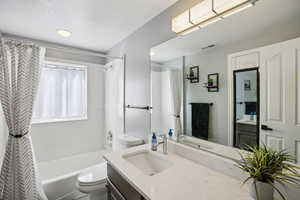 Bathroom featuring vanity, shower / bathtub combination with curtain, and a textured ceiling