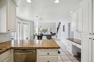 Kitchen featuring tasteful backsplash, stainless steel dishwasher, a peninsula, decorative light fixtures, and white cabinetry
