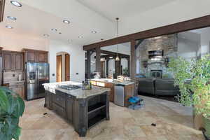 Kitchen with arched walkways, stainless steel appliances, decorative light fixtures, dark wood finish cabinetry, and beam ceiling