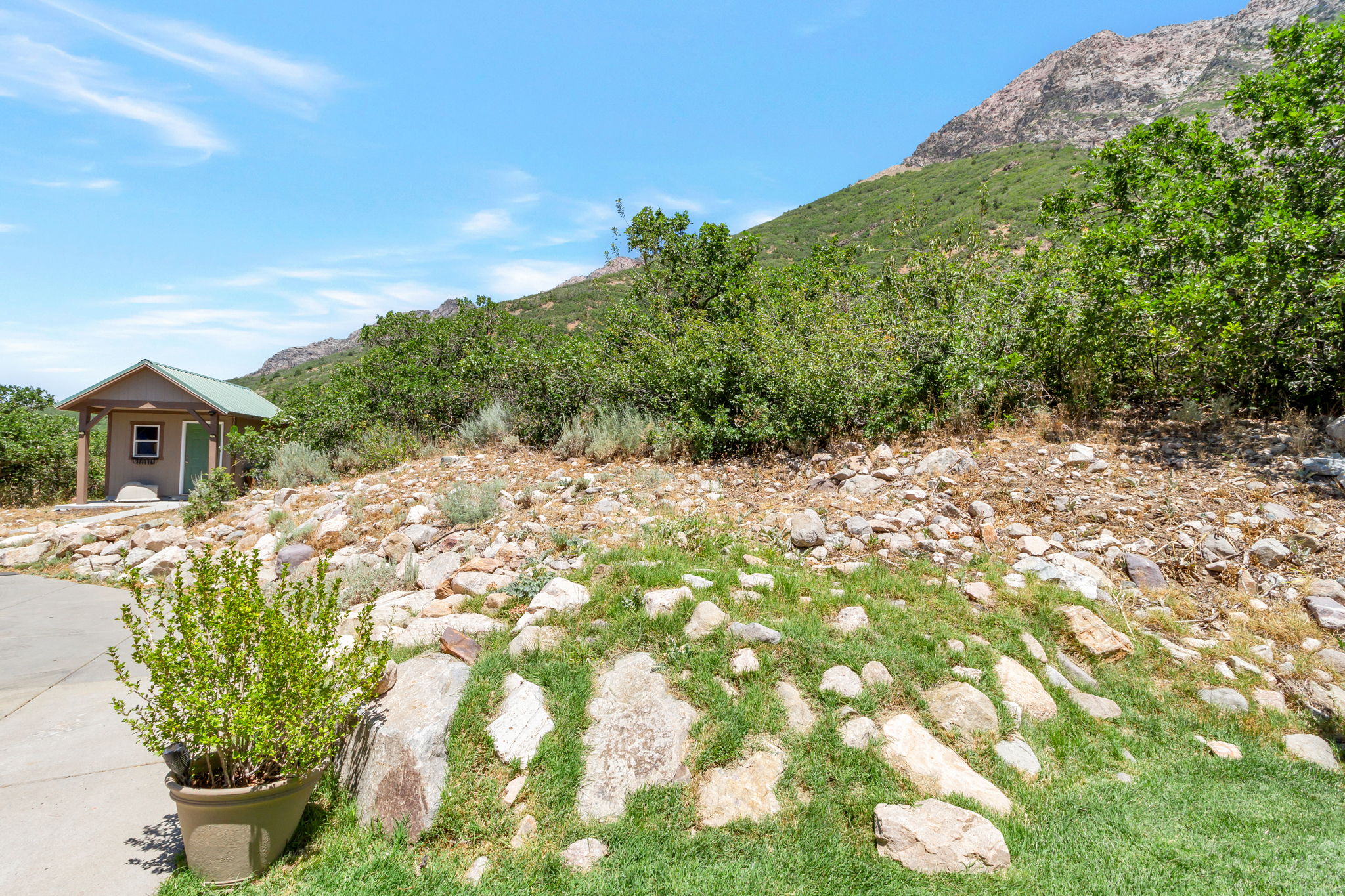 Mountainous terrain featuring a small outbuilding with a green metal roof, a paved surface, and natural rock landscaping