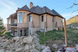 Rear view of house with stucco siding, stone siding, a patio, and a chimney