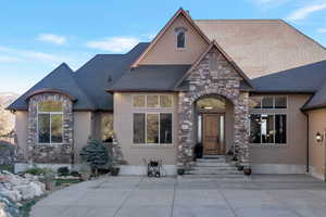 View of front of property featuring stone siding, stucco siding, entry steps, and a high end roof