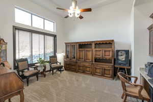 Home office featuring a ceiling fan, light colored carpet, and a high ceiling