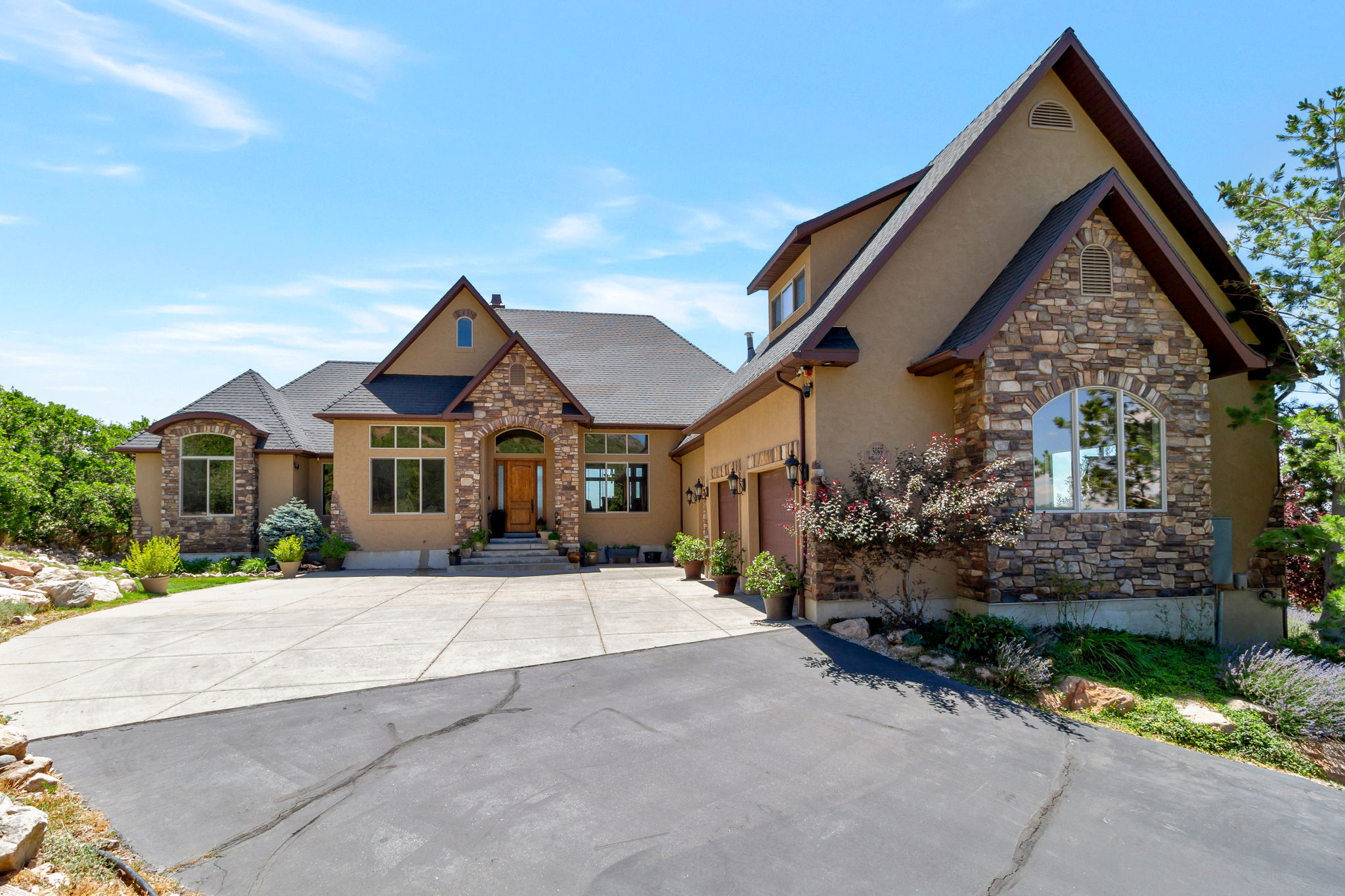 Stucco and stone facade home featuring a prominent arched entryway, multiple gabled rooflines, and a paved driveway leading to an attached three-car garage