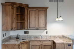 Kitchen featuring light stone counters, open shelves, wood finish cabinets, and pendant lighting