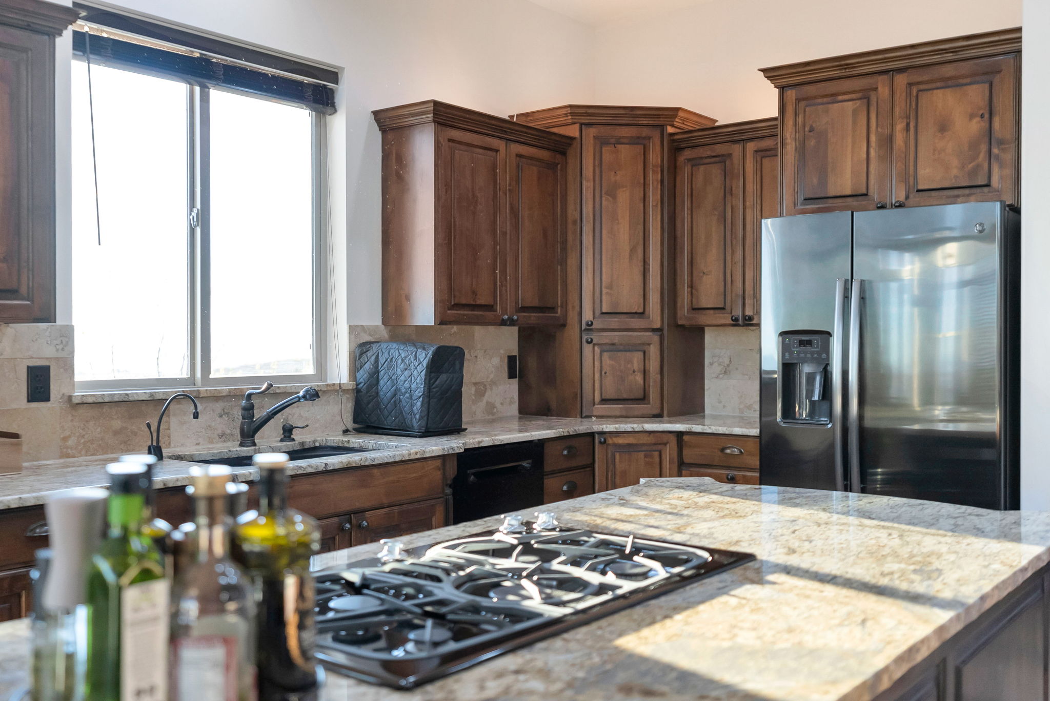 Kitchen with stainless steel fridge with ice dispenser, black gas cooktop, decorative backsplash, light stone counters, and dark wood finish cabinets