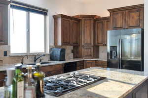 Kitchen with stainless steel fridge with ice dispenser, black gas cooktop, decorative backsplash, light stone counters, and dark wood finish cabinets