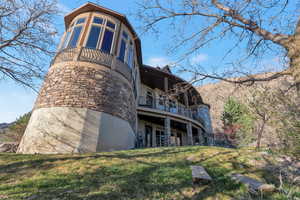 Back of property with a balcony, stone siding, a yard, stucco siding, and a patio