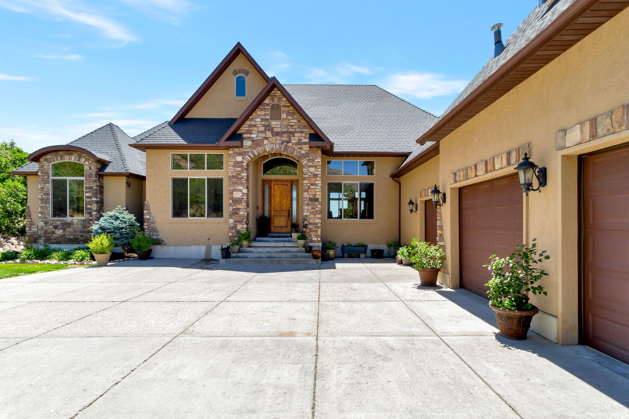 Stucco and stone facade home featuring a prominent arched entryway, multiple large windows, and an attached two-car garage with individual brown doors