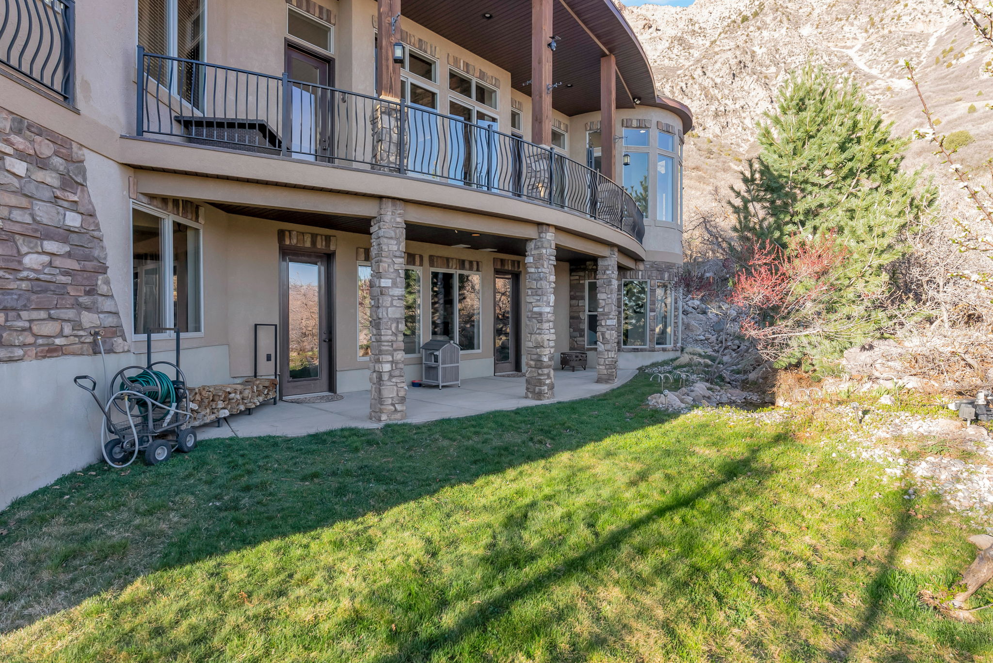 Back of property featuring stucco siding, a balcony, a patio area, stone siding, and a yard