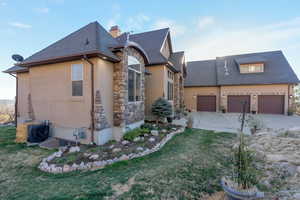 View of side of property with stucco siding, driveway, stone siding, a yard, and a chimney