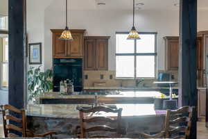 Kitchen with light stone countertops, decorative backsplash, hanging light fixtures, and a kitchen island with sink