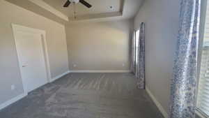 Empty room featuring a raised ceiling, ceiling fan, and carpet flooring