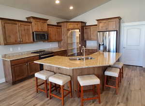 Kitchen featuring a kitchen bar, light stone countertops, stainless steel appliances, vaulted ceiling, and a center island with sink